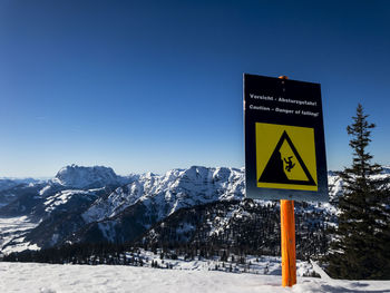 Information sign on snowcapped mountain against clear blue sky