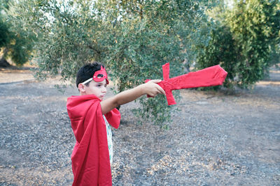 Child disguised as a red superhero points his sword at the ghosts