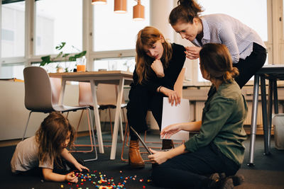 Female colleagues discussing over laptop by boy playing on floor at creative office