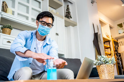 Young man wearing mask using hand sanitizer at home