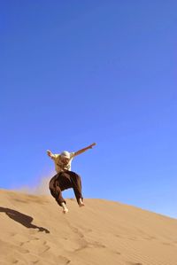 Low angle view of man jumping on sand against clear sky