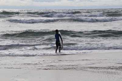 Rear view of man walking on beach against sky