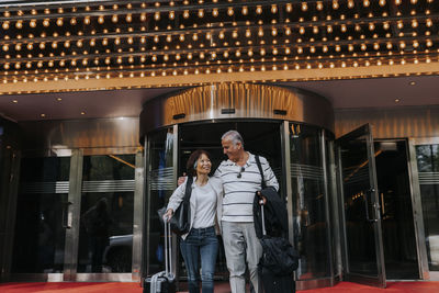 Smiling male and female senior friends walking in front of illuminated movie theater