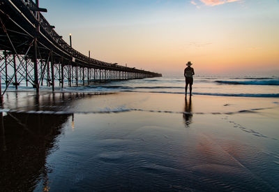 Man standing on pier over sea against sky during sunset