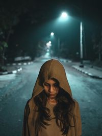 Portrait of young woman standing against illuminated light at night