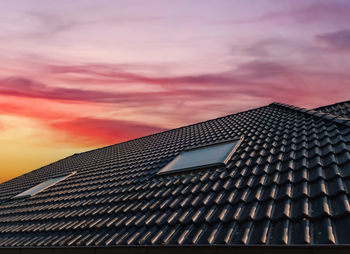 Open roof window in velux style with black roof tiles during sunset