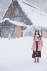 Woman holding umbrella standing against built structure during winter
