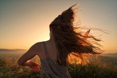 Rear view of girl standing against sky during sunset