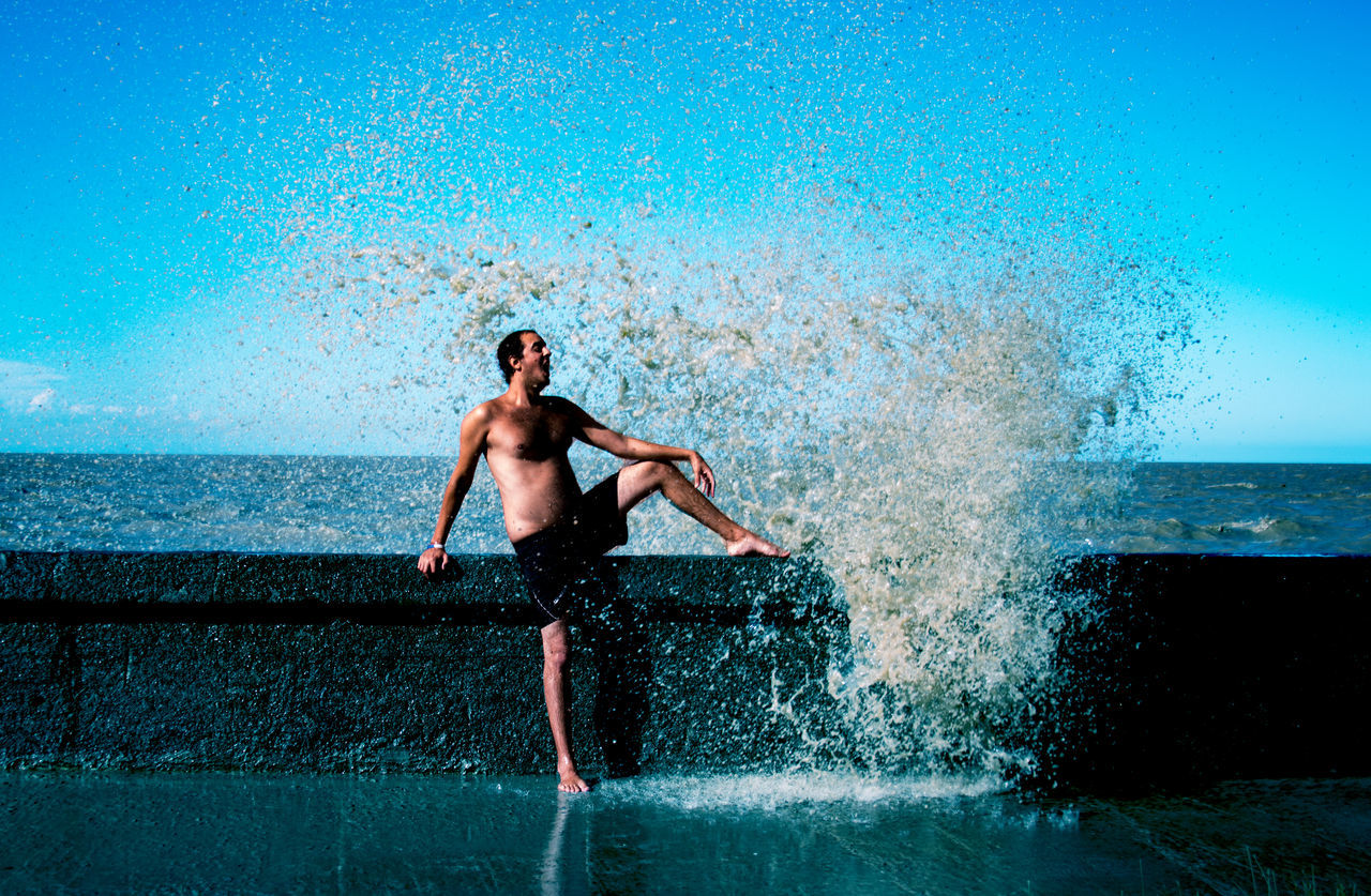 FULL LENGTH OF SHIRTLESS MAN STANDING IN SWIMMING POOL