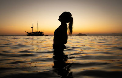 Silhouette woman standing in sea against sky during sunset