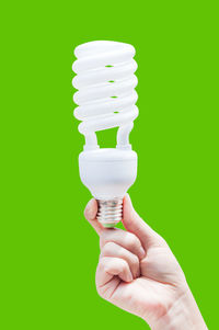 Close-up of person holding light bulb over green background