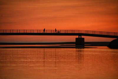 Silhouette bridge over river against sky during sunset