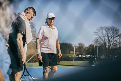 Senior male friends with rackets standing at tennis court