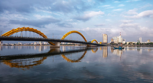 Bridge over river by buildings against sky in city