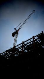 Low angle view of silhouette crane against sky