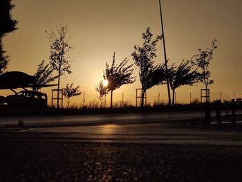 Silhouette trees by road against sky during sunset