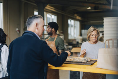 Male and female owners assisting customers buying fresh bread from bakery