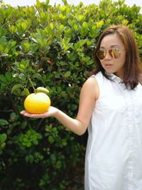 Woman holding fruit while standing against plants