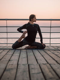 Full length of man sitting on pier against sky during sunset