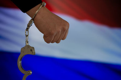 Cropped hand of male criminal with handcuffs against dutch flag