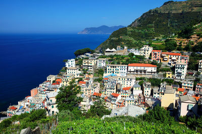 Buildings on mountain at manarola by sea against clear blue sky