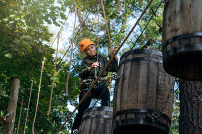 Well equipped teenage boy in outdoor passing obstacle course. active recreation in high rope park