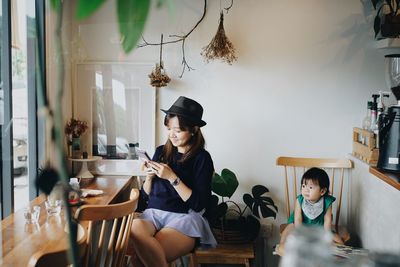 Mother using mobile phone with daughter in cafe