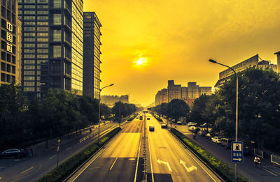 City street by buildings against sky during sunset