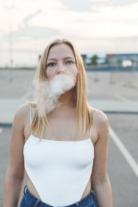 Blonde woman in city with electronic cigar vaping