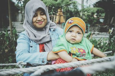 Smiling woman holding daughter amidst ropes in park