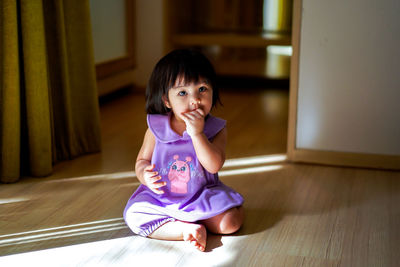 Portrait of cute girl sitting on hardwood floor at home