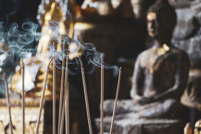 Close-up of incense sticks against statue