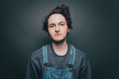 Portrait of confident young man wearing overalls on gray background