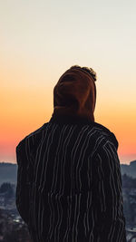 Rear view of man standing at beach against sky during sunset