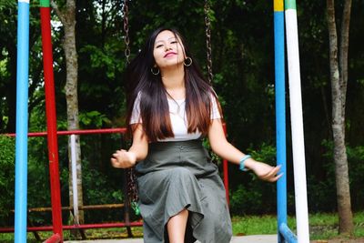 Portrait of young woman sitting on swing at playground