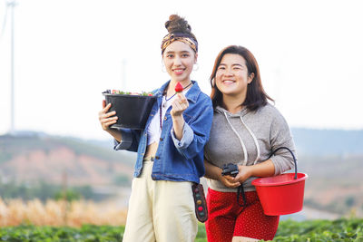 Portrait of smiling young women with strawberries against sky