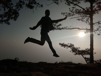 Silhouette man jumping on field against sky during sunset