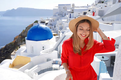 Portrait of fashionable woman in red dress and hat visiting a picturesque greek island