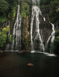 Woman swimming in river against waterfall