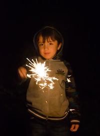 Portrait of cute boy holding sparkler at night