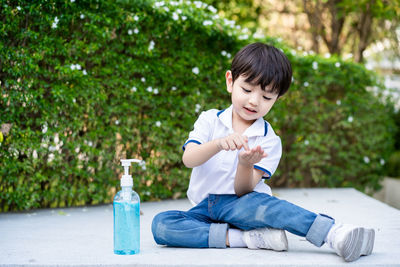 Full length of cute boy cleaning hands with sanitizer outdoors