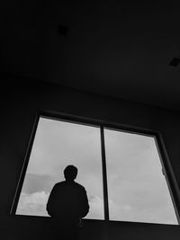 Rear view of man looking through window while standing in room