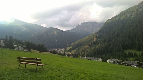 Empty bench on field by mountains against sky