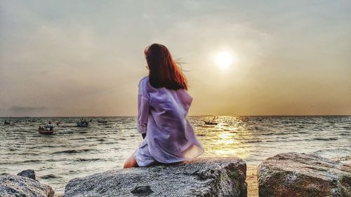 Rear view of woman looking at sea against sky during sunset