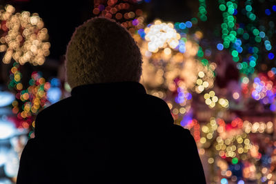 Rear view of woman standing against illuminated christmas tree at night