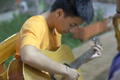 Teenage boy playing guitar while sitting outdoors