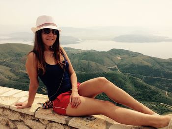 Young woman sitting on retaining wall against mountains