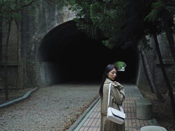 Side view of woman standing on footpath against tunnel