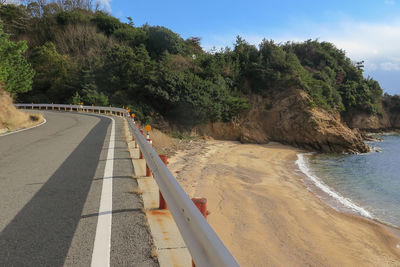 Road by trees, sandy beach against sky