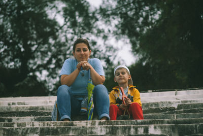 Full length of father and daughter sitting on tree